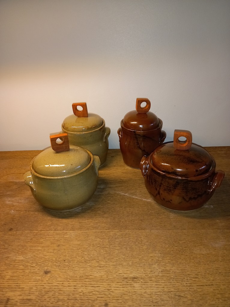 Een groep van vier handgemaakte keramische potten, twee in een groene en twee in een bruine tint, staan op een houten tafel.